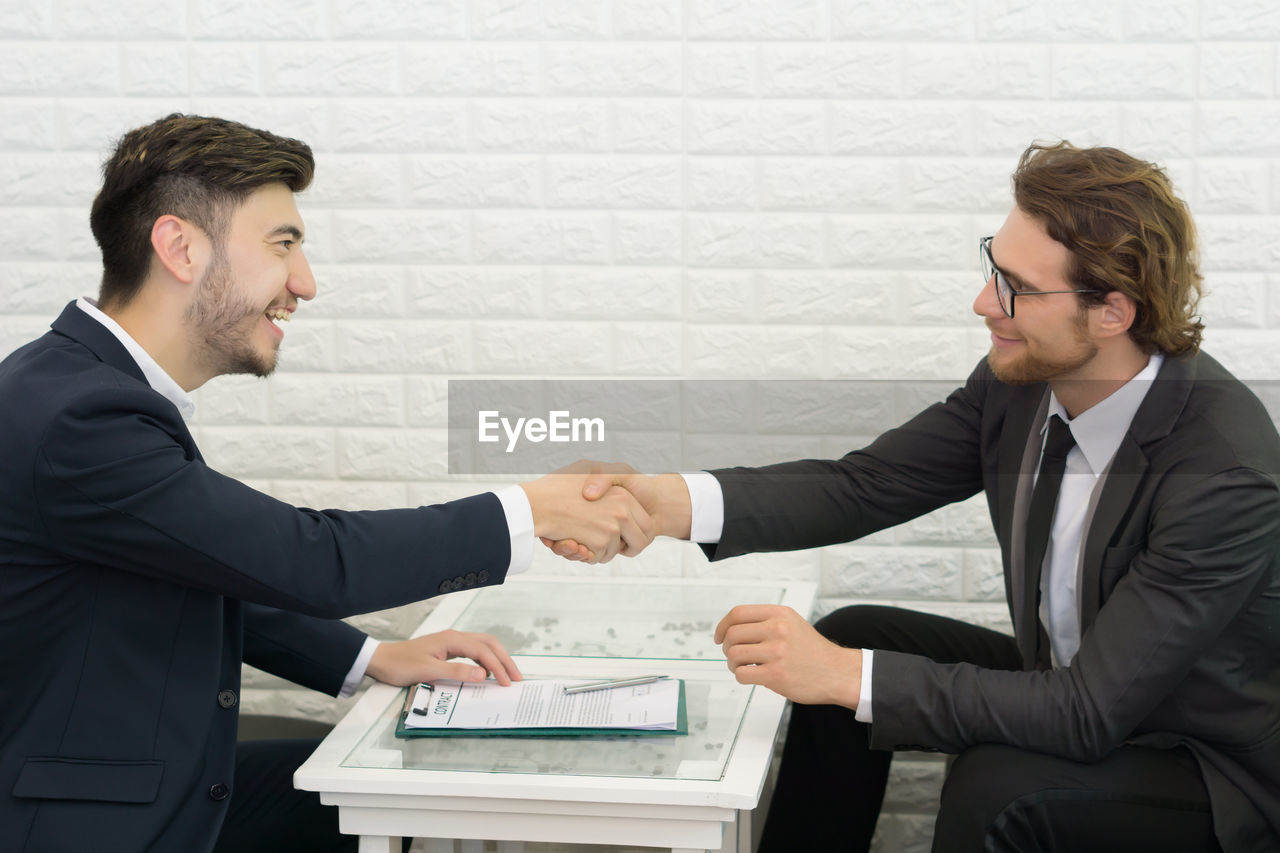 Businessmen shaking hands while sitting at table in office