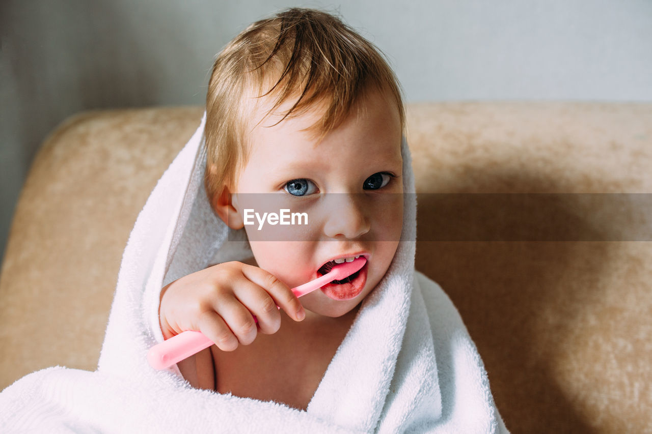 Cute child in big white towel. she brushes his teeth with toothbrush.