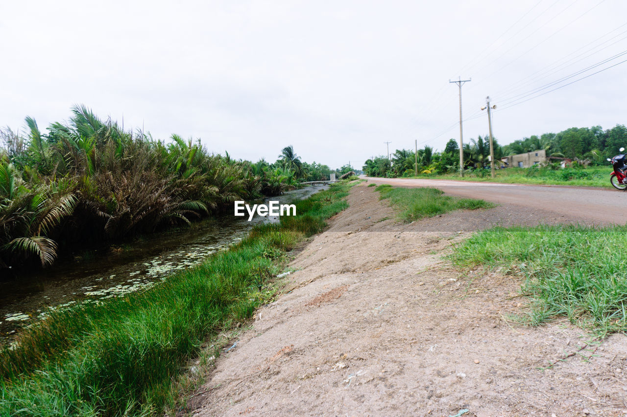 DIRT ROAD AMIDST PLANTS AND TREES AGAINST SKY