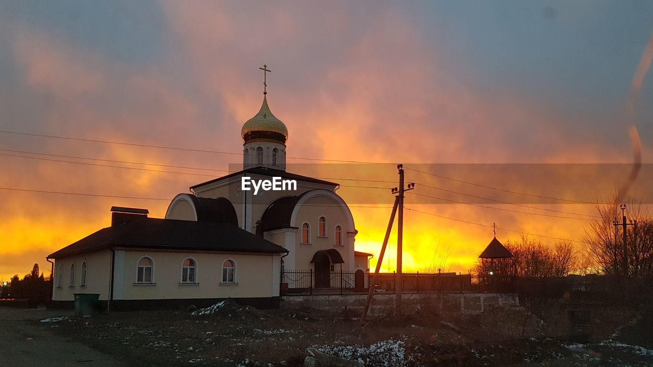 CHURCH BY BUILDING AGAINST ORANGE SKY