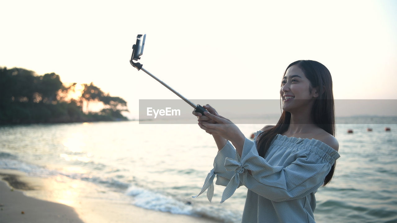 YOUNG WOMAN USING SMART PHONE AT BEACH