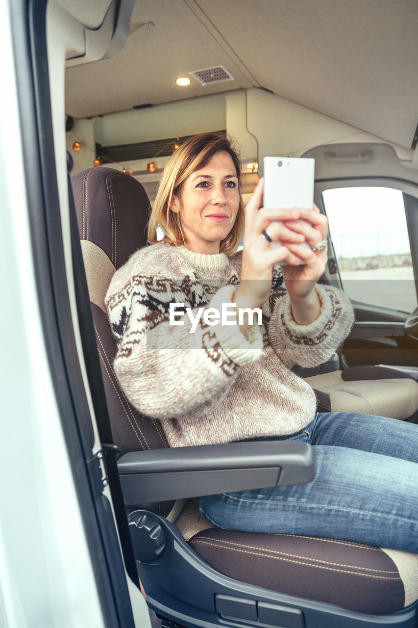 Woman taking picture with cell phone sitting in a camper van