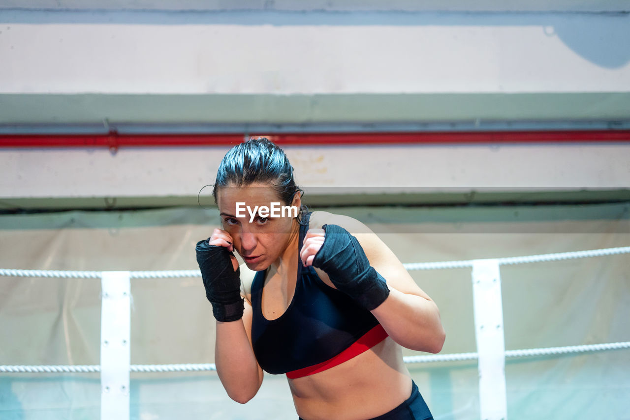 Female boxer ready to kick with black boxing bandage on hands in gym.