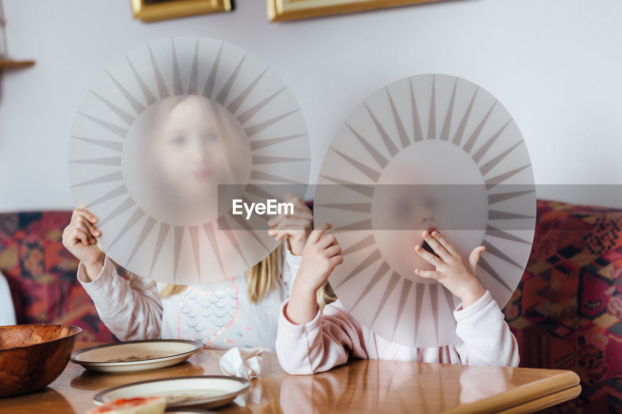 Siblings covering face with plates at home