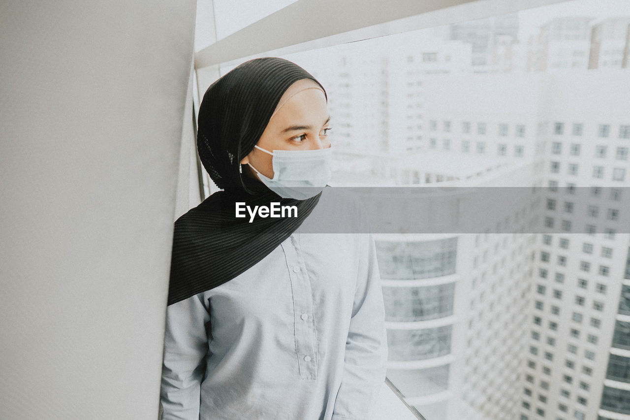 Portrait of young woman wearing facemask standing against wall 