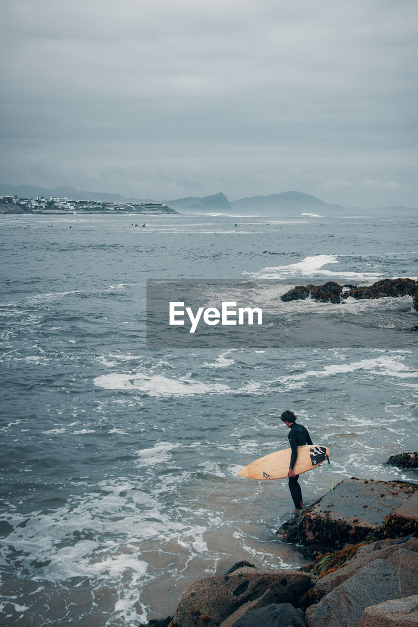 Young man surfing in sea against cloudy sky