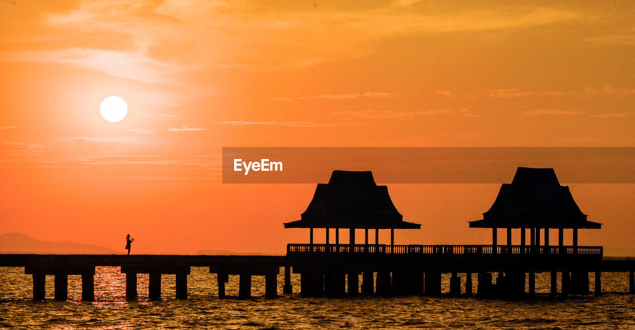 Silhouette wooden posts in sea against orange sky