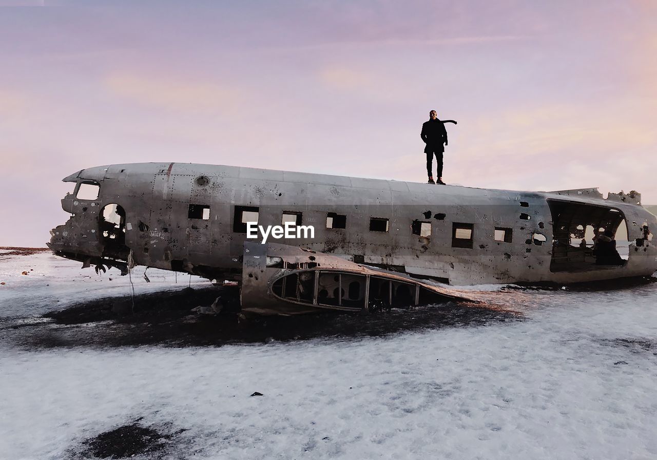 Man standing on abandoned airplane against sky during winter