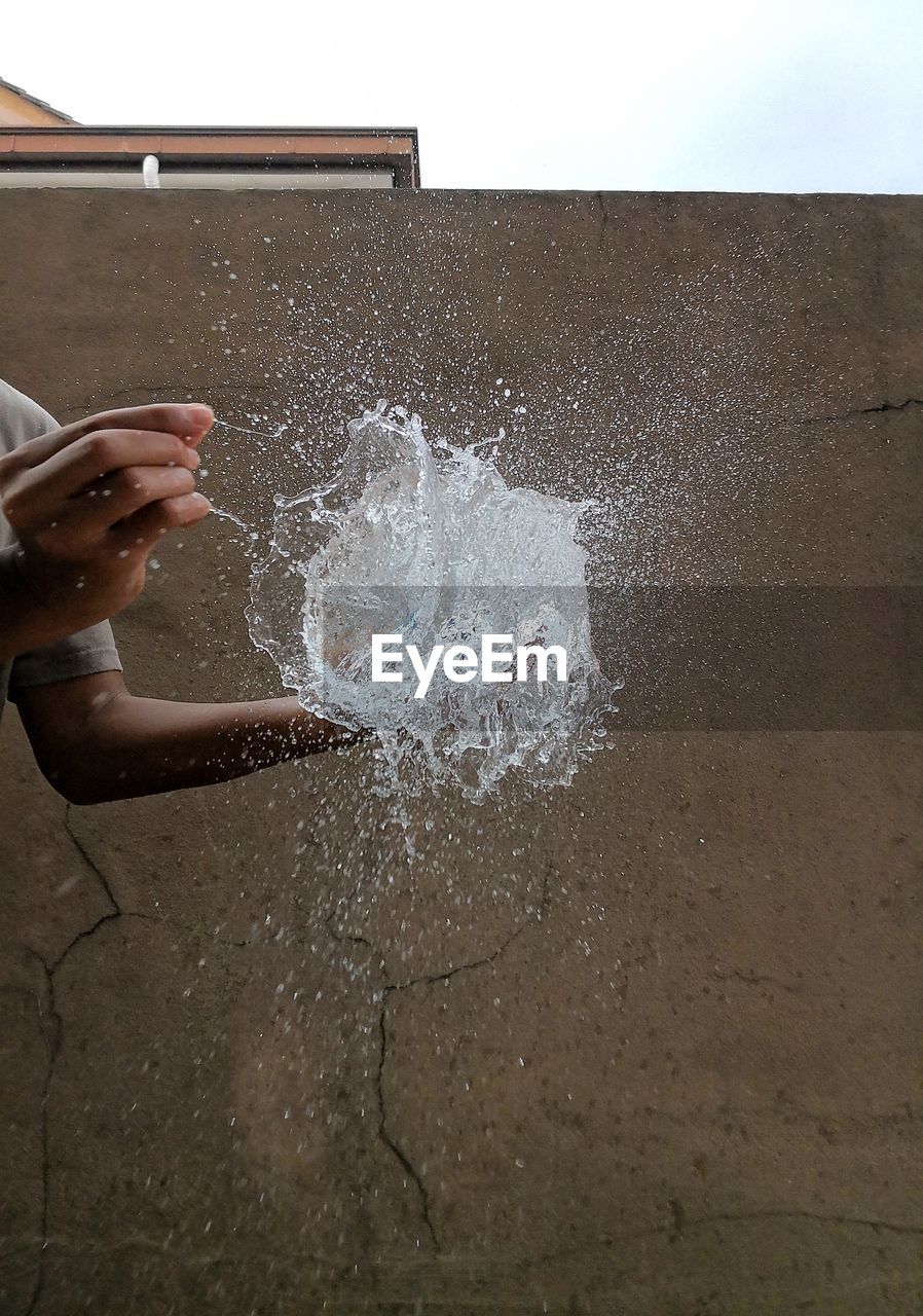 Cropped hands of person exploding water bomb against wall