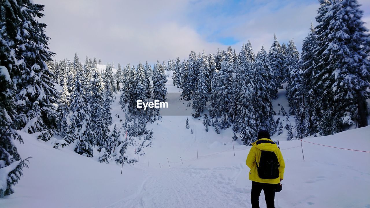 Rear view of man walking on snow covered mountain against sky