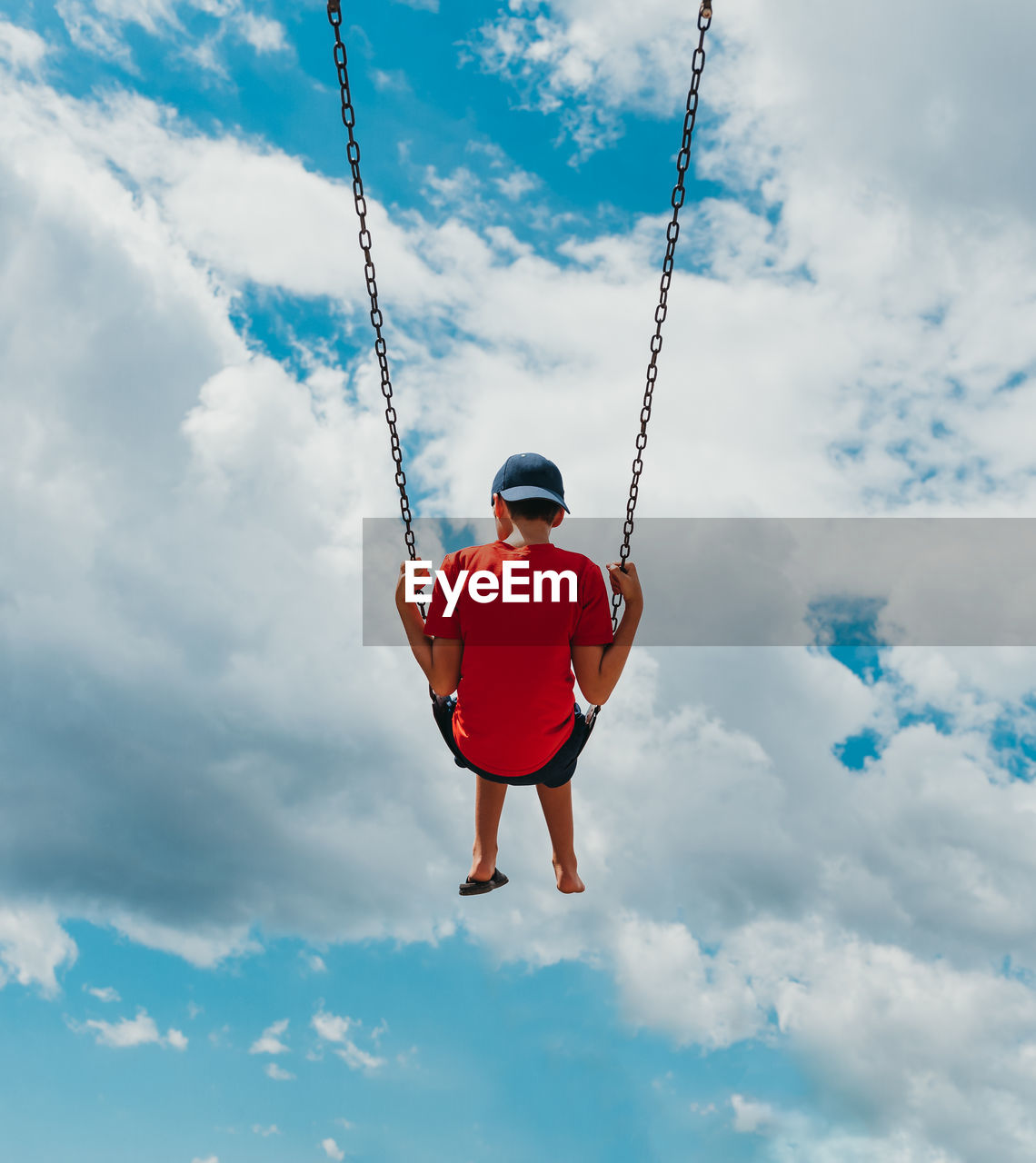 Rear view of boy on a swing with only cloudy sky in the background.