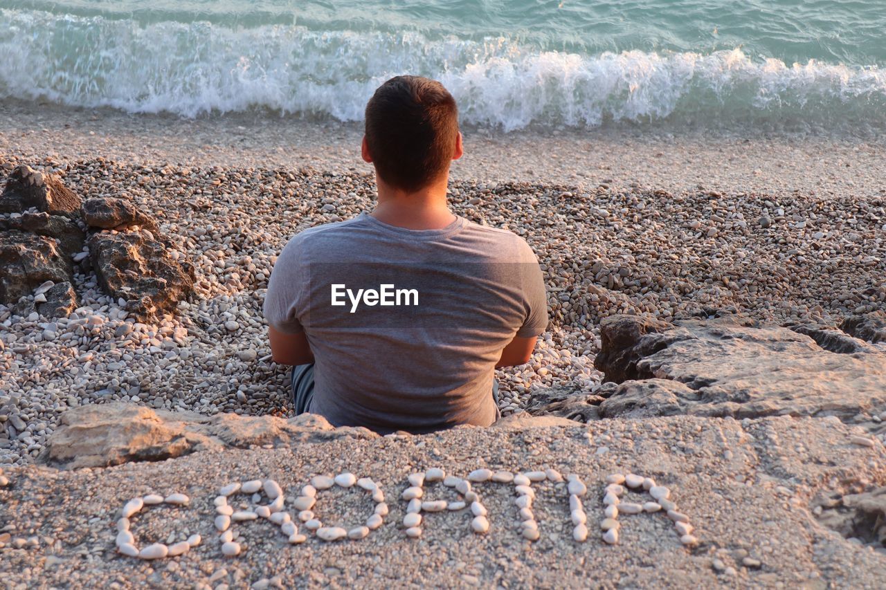 Croatia texts made by pebble behind man sitting at beach