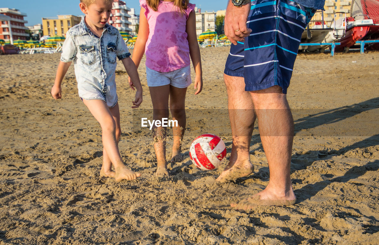 Father playing soccer with son and daughter on sand at beach