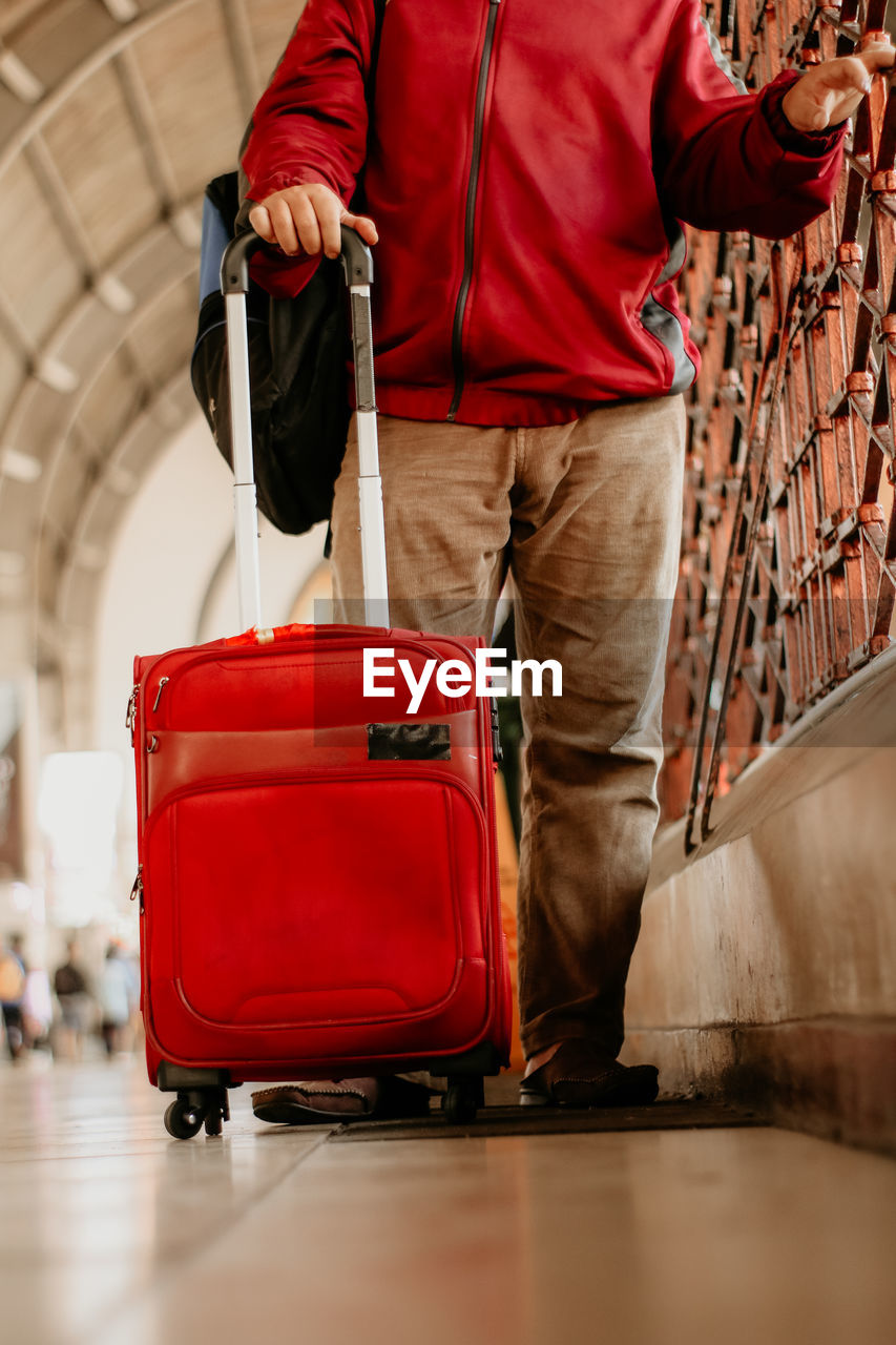 Low section of man with red suitcase at airport