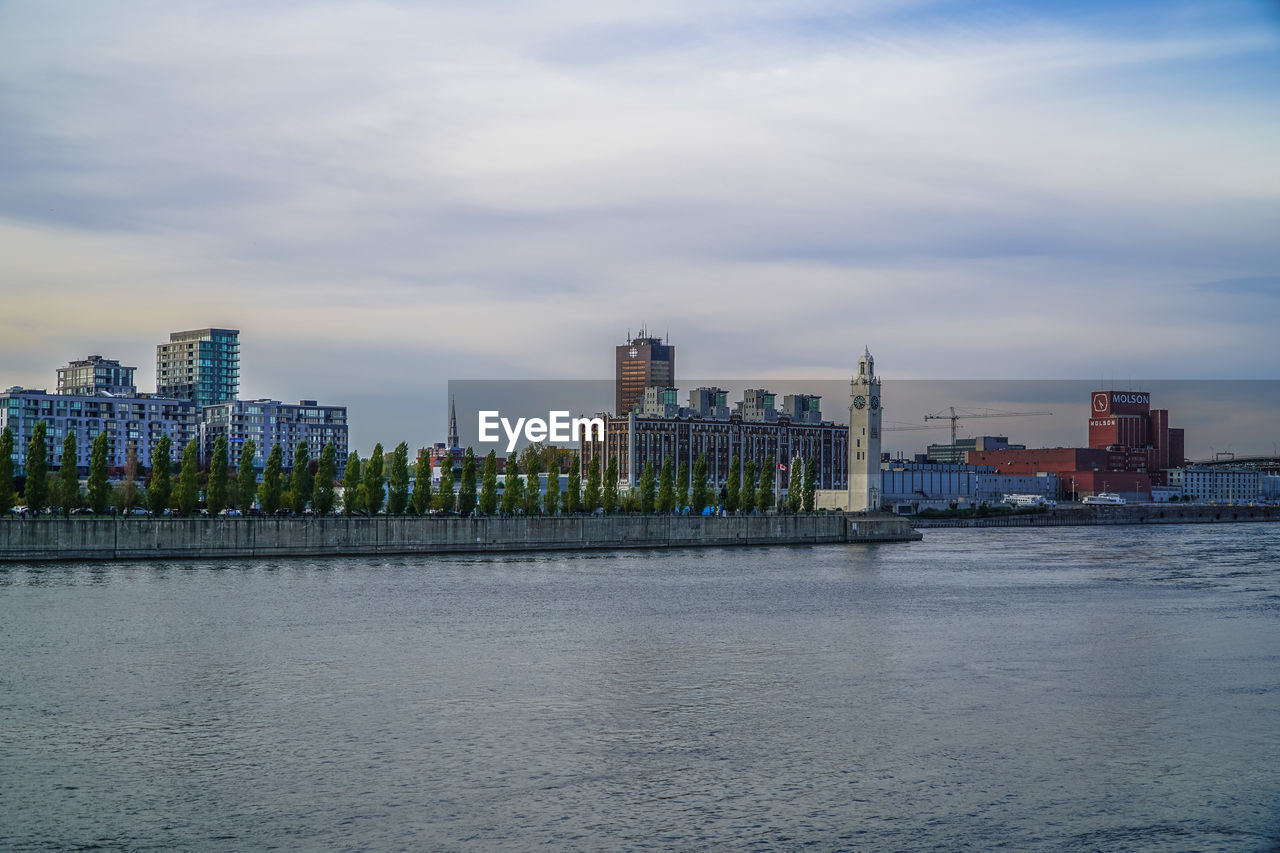 City at waterfront against cloudy sky