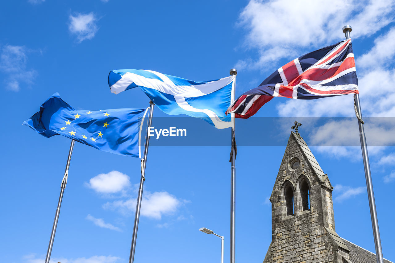 Low angle view of european union, scotland and great britain flags flying against blue sky.