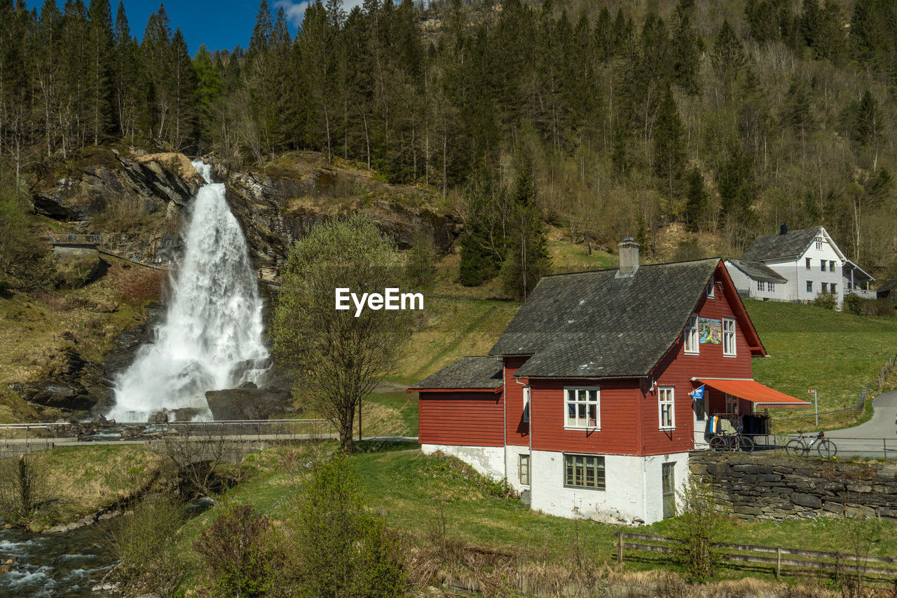 architecture, built structure, building exterior, building, plant, house, water, mountain range, mountain, tree, nature, land, scenics - nature, wilderness, landscape, no people, environment, beauty in nature, residential district, forest, waterfall, rural area, day, motion, outdoors, travel destinations, sky, hut, non-urban scene, grass, rural scene