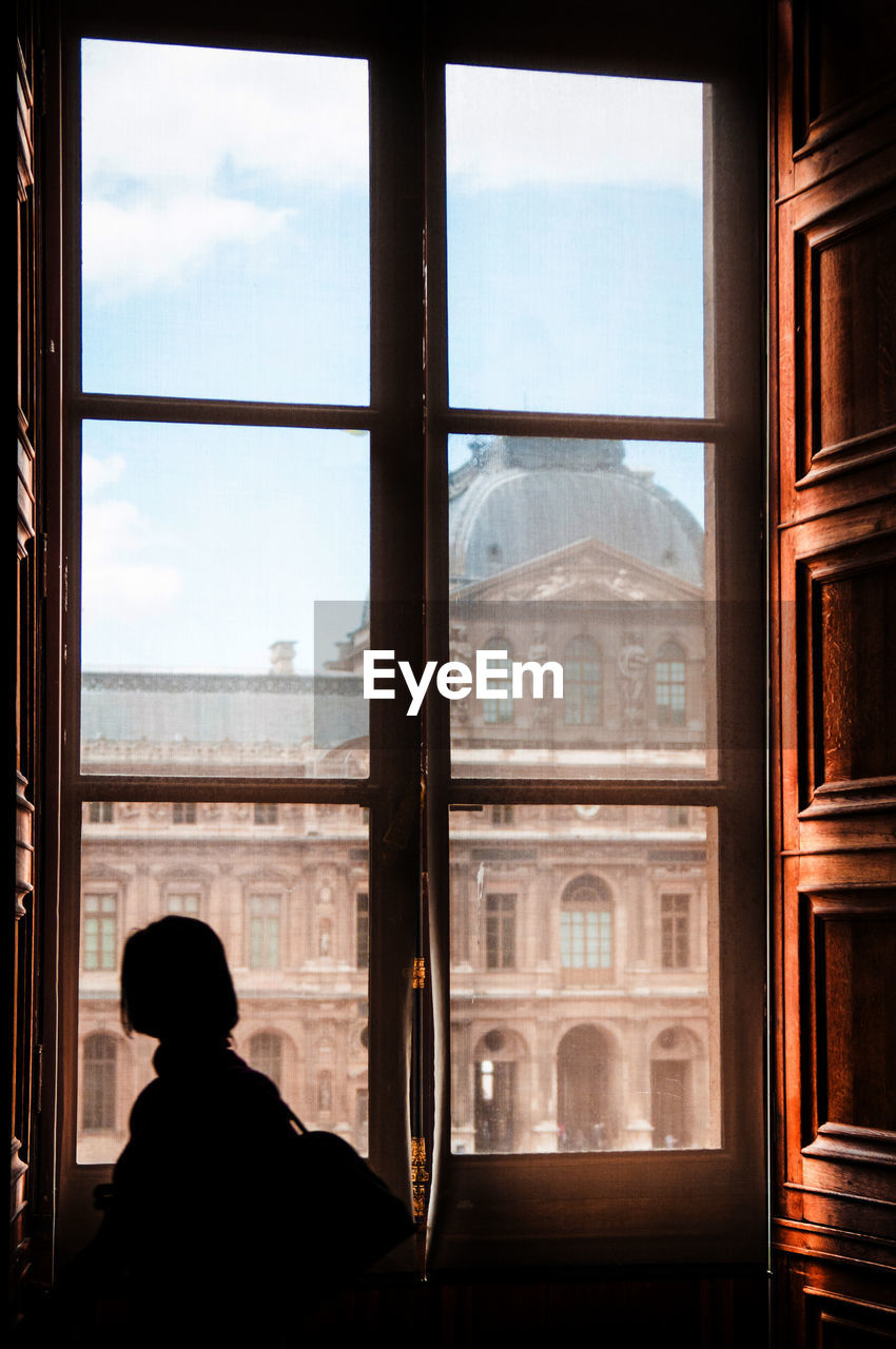 REAR VIEW OF WOMAN LOOKING THROUGH WINDOW