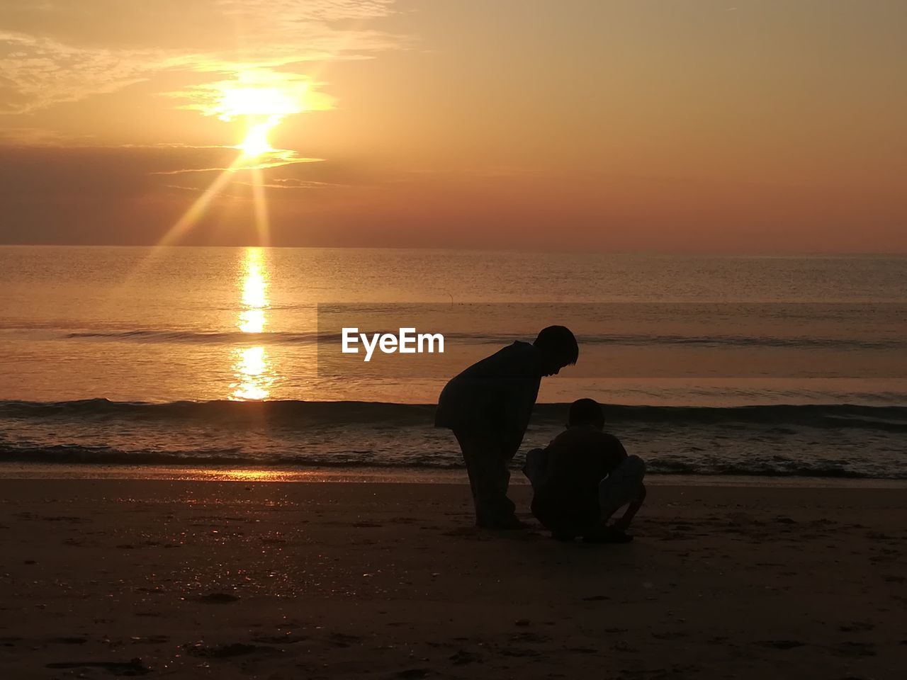 Boys on beach against sky during sunset