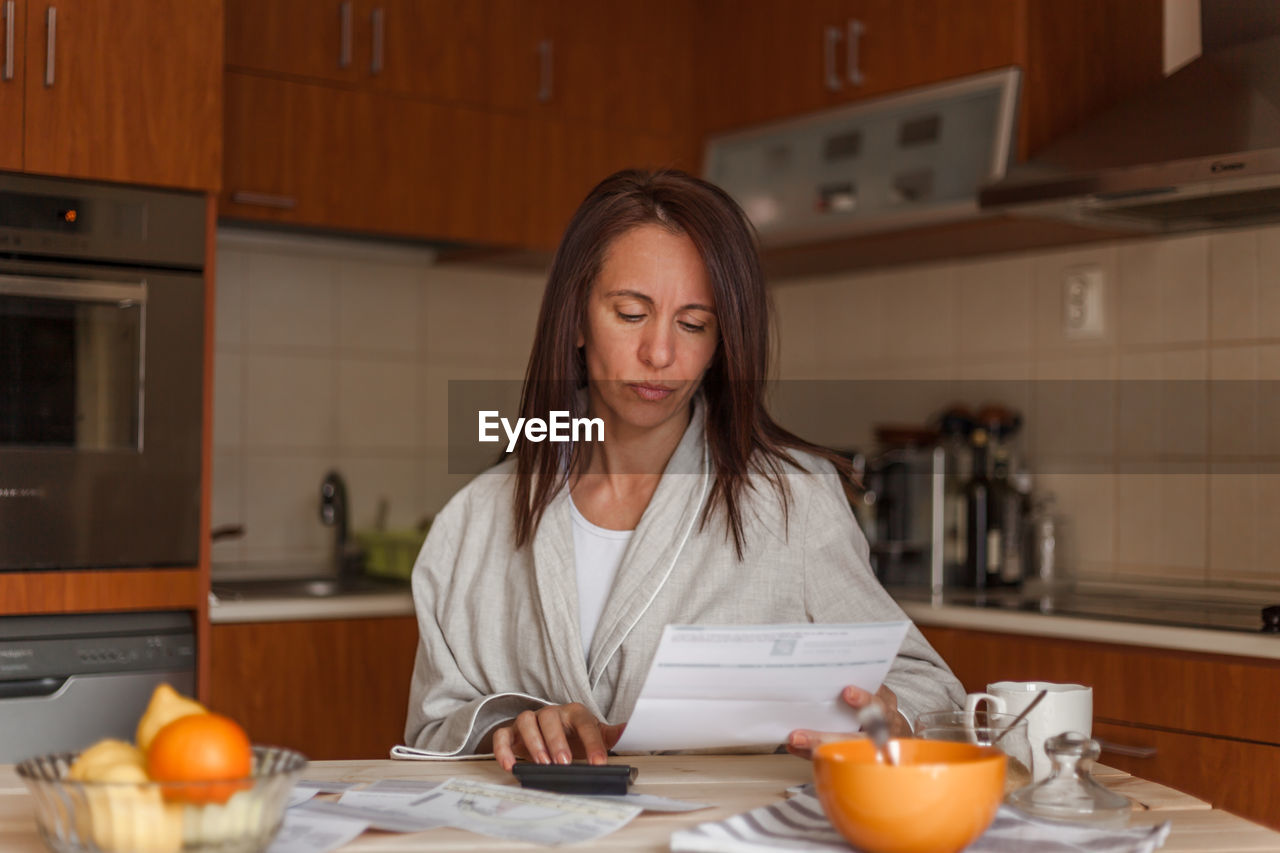 Woman reading document while having breakfast at home