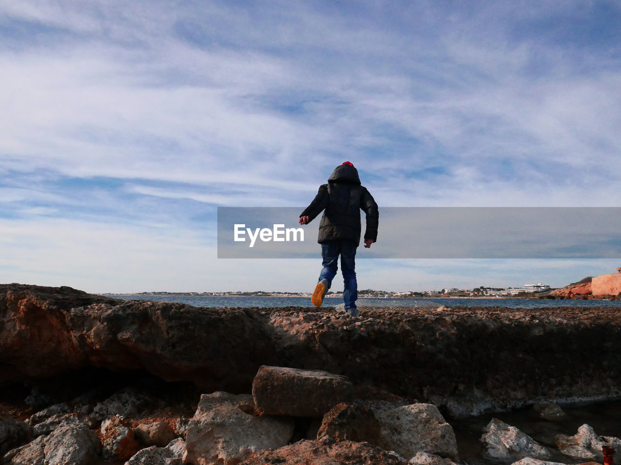 Rear view of boy walking on rocks at beach