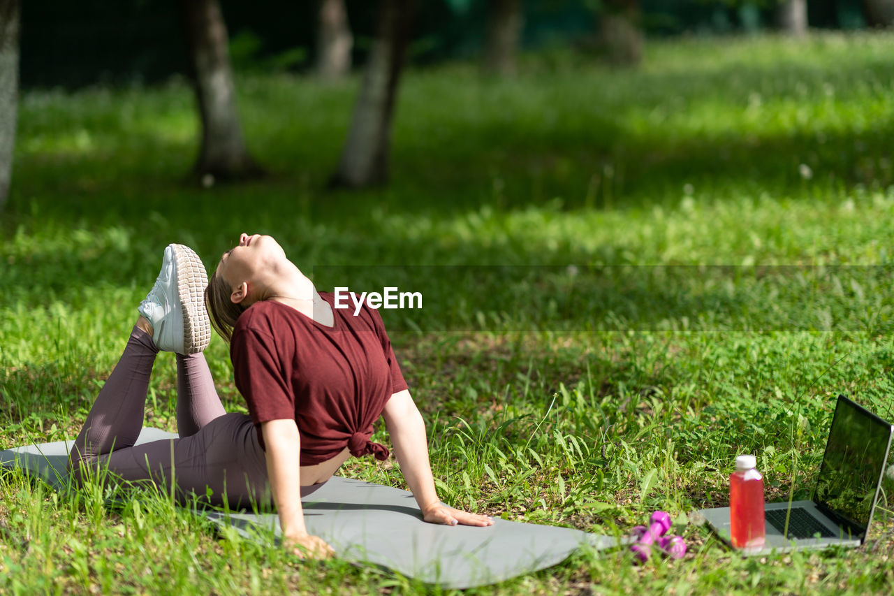 Young girl having online workout outdoors using laptop. pilates or yoga video lesson on internet.