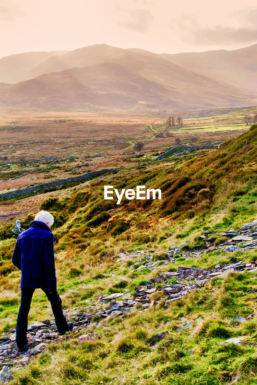 REAR VIEW OF MAN LOOKING AT MOUNTAIN LANDSCAPE