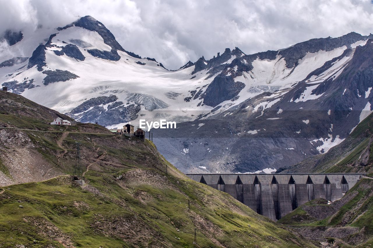 View of dam amidst snowcapped mountains against cloudy sky