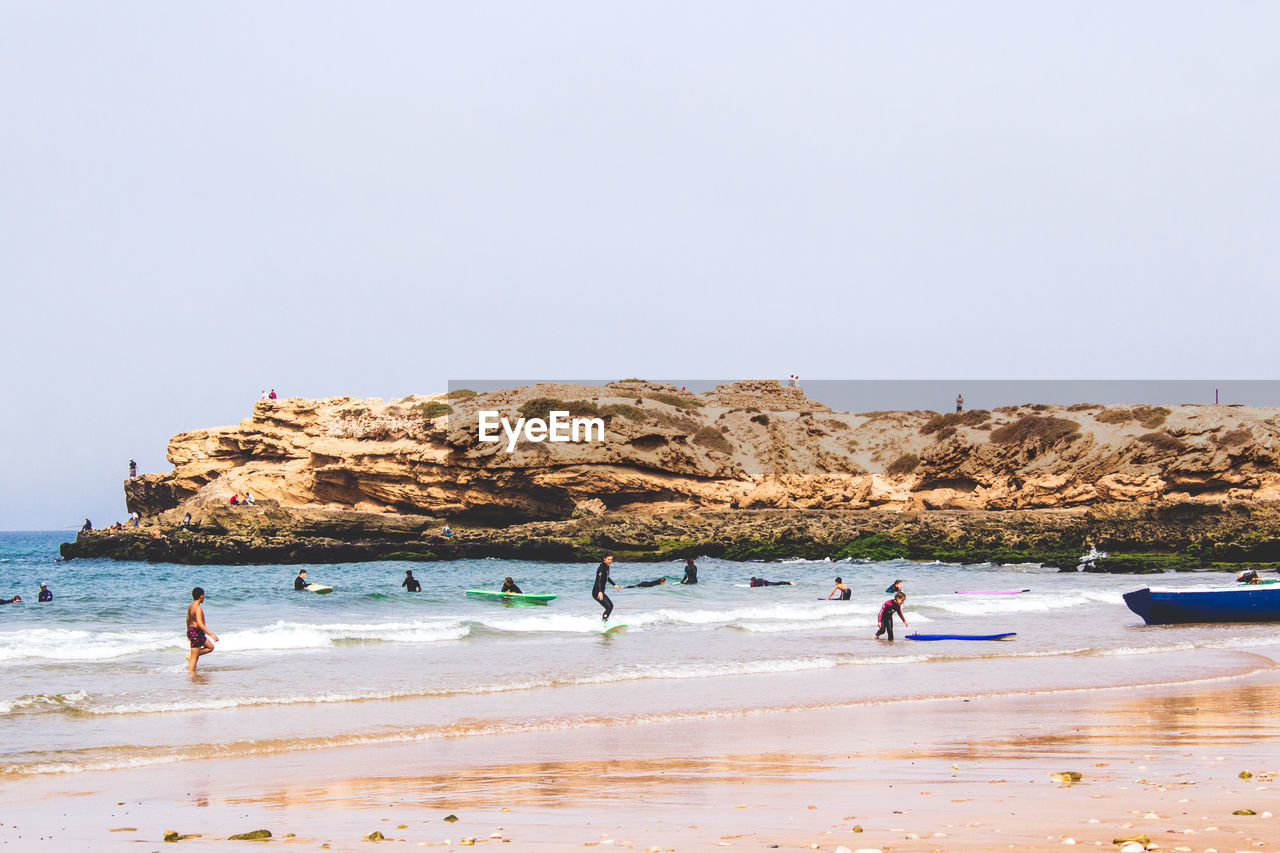 PEOPLE ENJOYING ON BEACH AGAINST CLEAR SKY