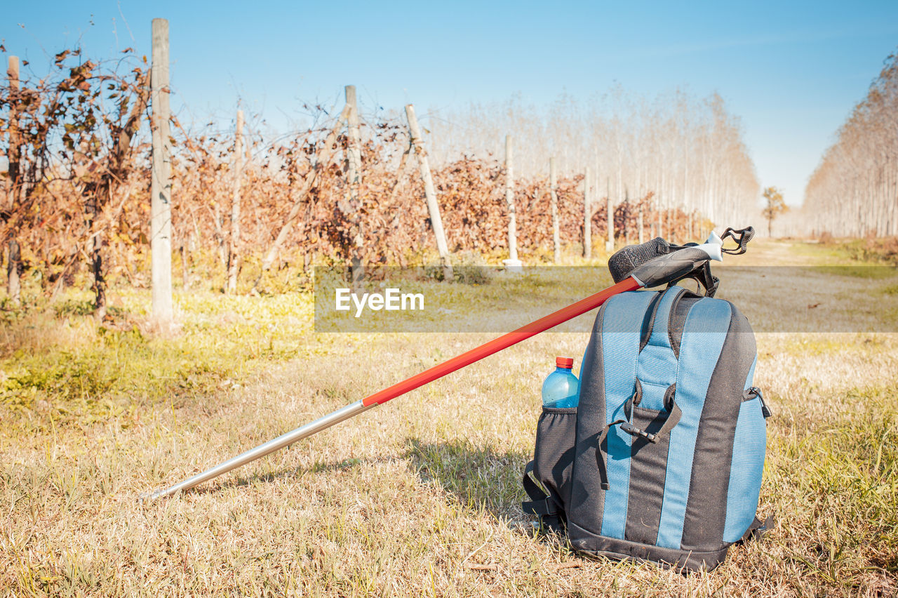 Backpack with hiking poles on field against sky
