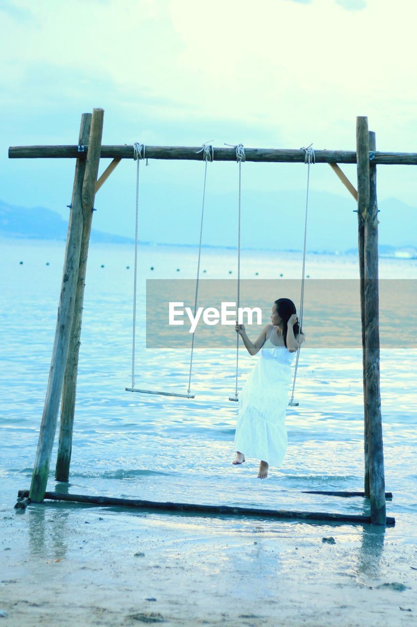 REAR VIEW OF WOMAN STANDING AT SEA SHORE AGAINST SKY