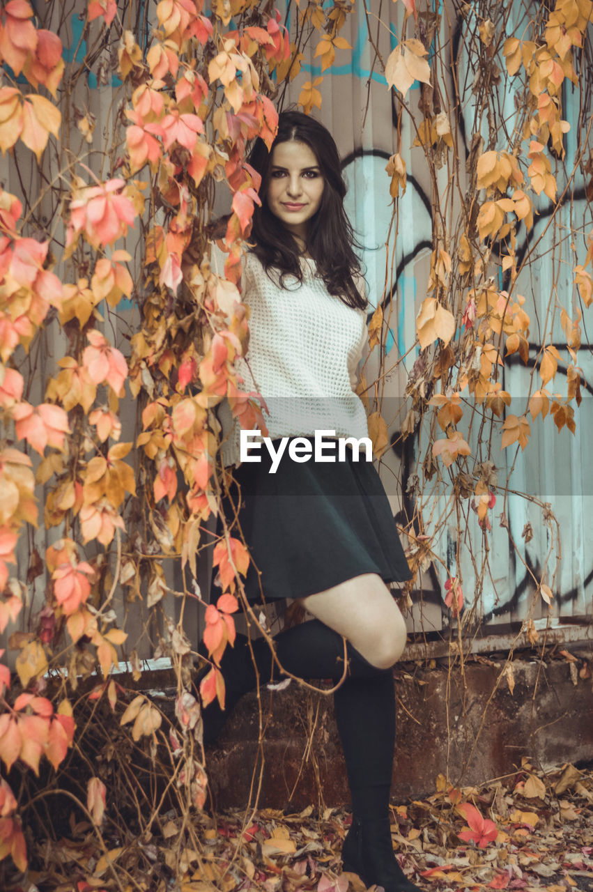 Portrait of young woman standing amidst creeper plants during autumn