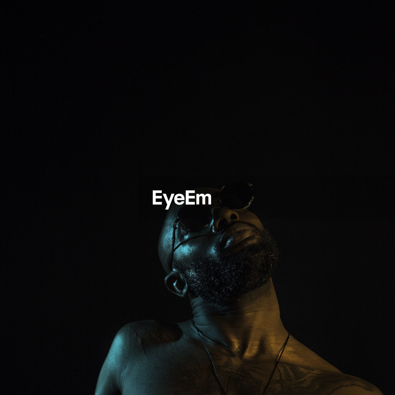 CLOSE-UP OF MAN WEARING EYEGLASSES AGAINST BLACK BACKGROUND AGAINST GRAY