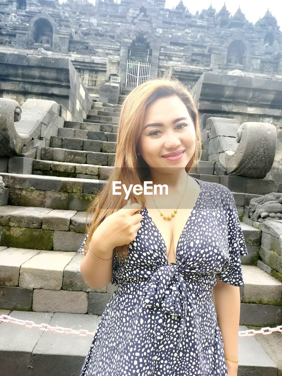 PORTRAIT OF SMILING YOUNG WOMAN STANDING OUTDOORS