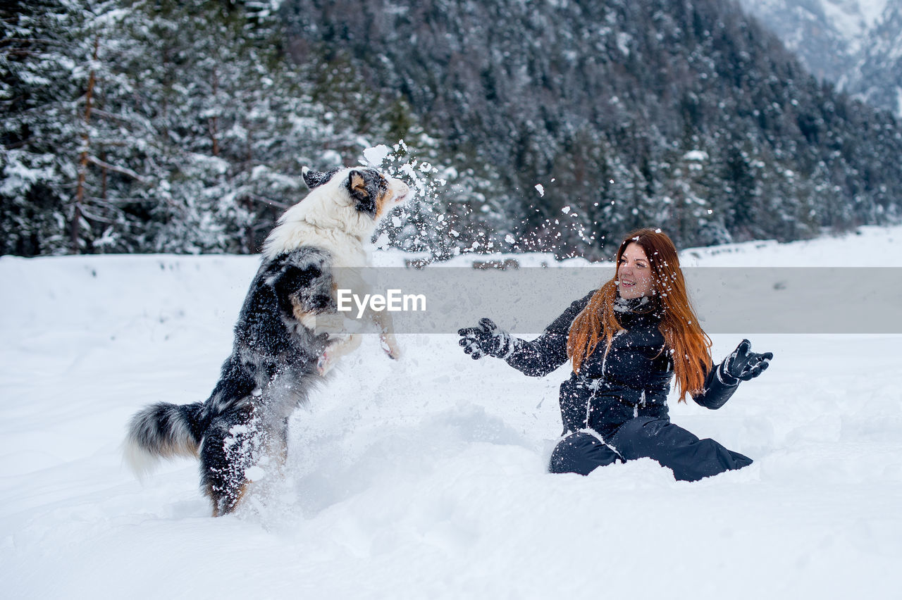 Cheerful woman playing with dog on snow covered field