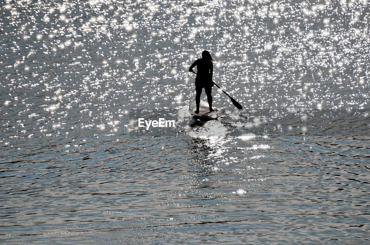 Silhouette man paddleboarding in sea