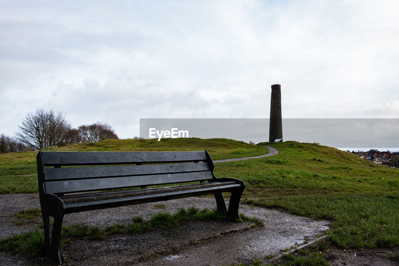 Empty bench on field against sky