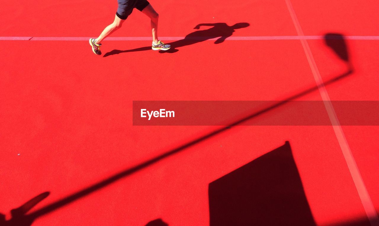 Low section of man running on red court during sunny day