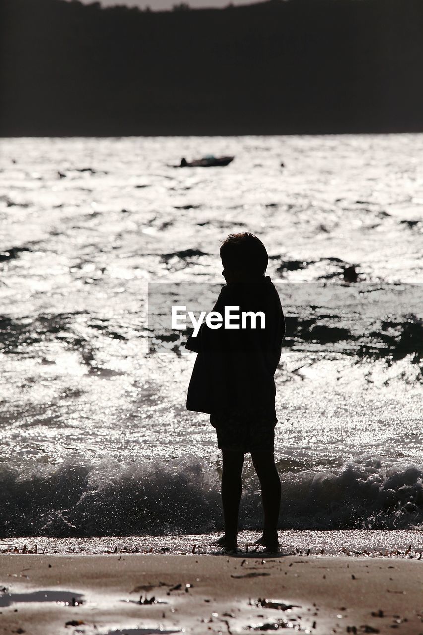 Silhouette of boy standing on shore against seascape