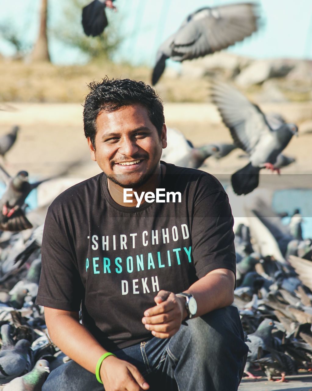 Portrait of smiling young man crouching against pigeons on sunny day