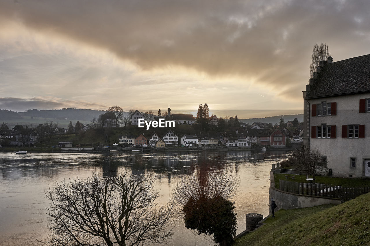 Scenic view of river by buildings against sky during sunset