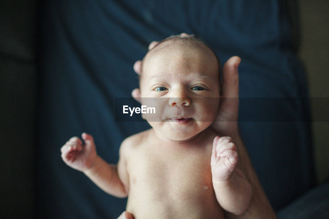 Overhead portrait of newborn baby boy held by father in hospital