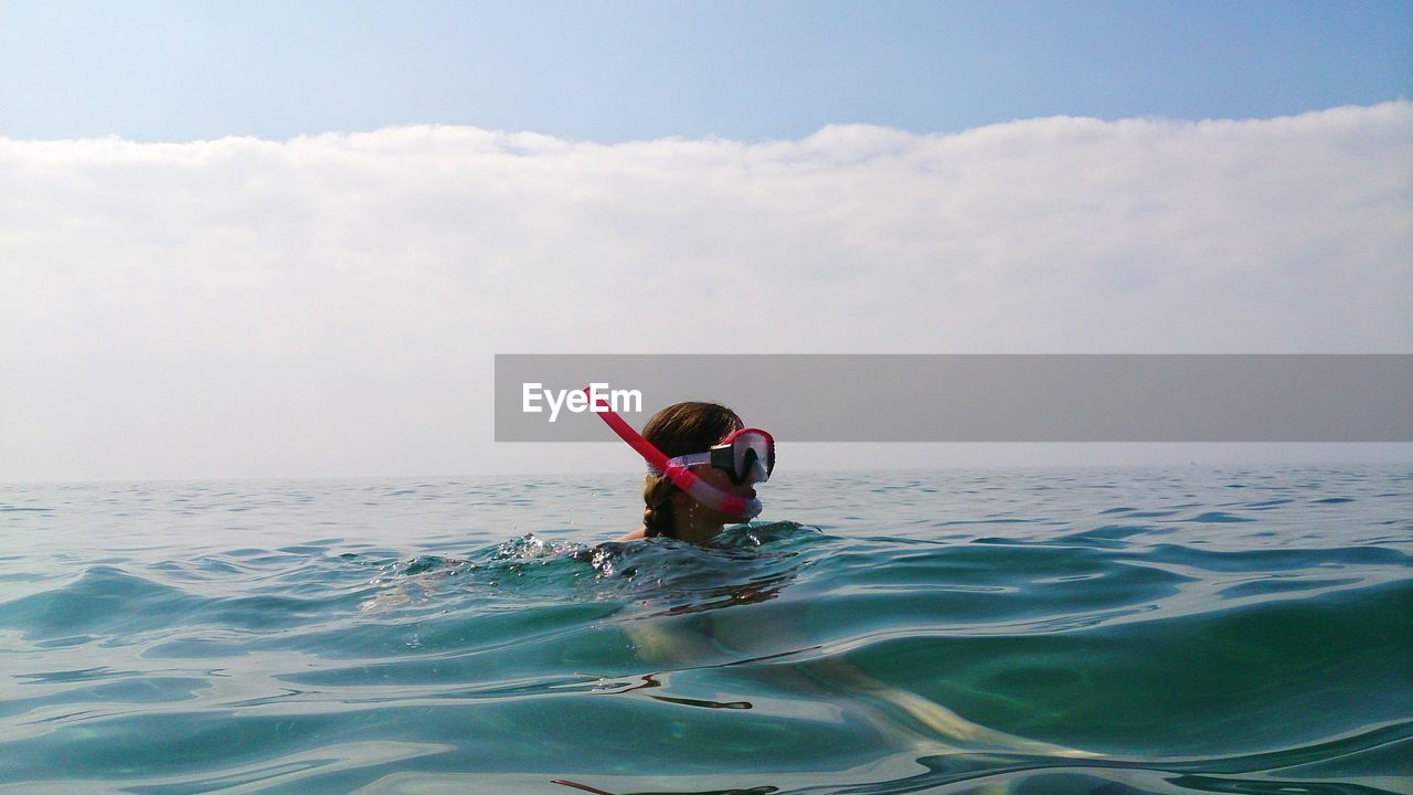 Woman with snorkel swimming in sea against cloudy sky