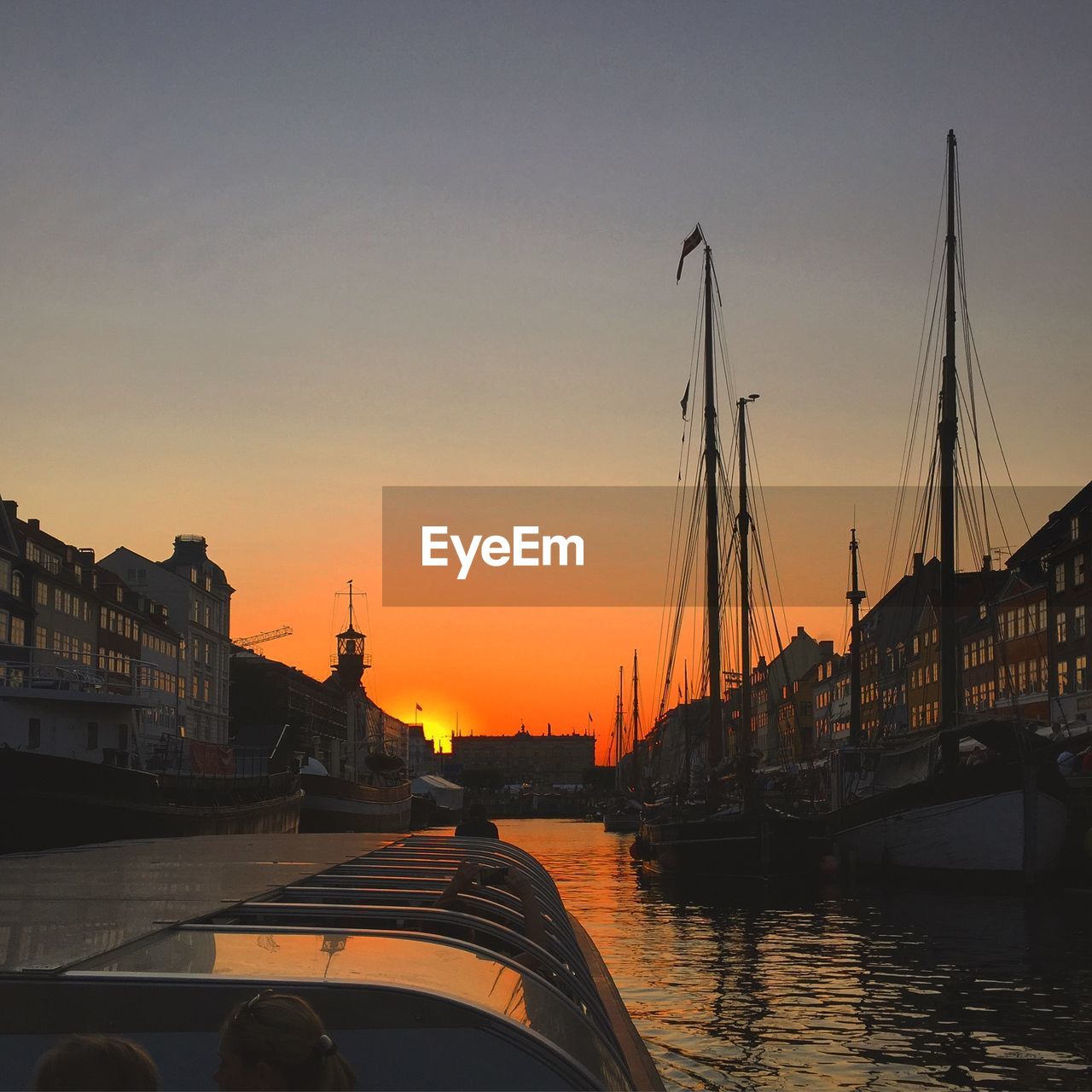 Nautical vessel on river amidst buildings against sky during sunset