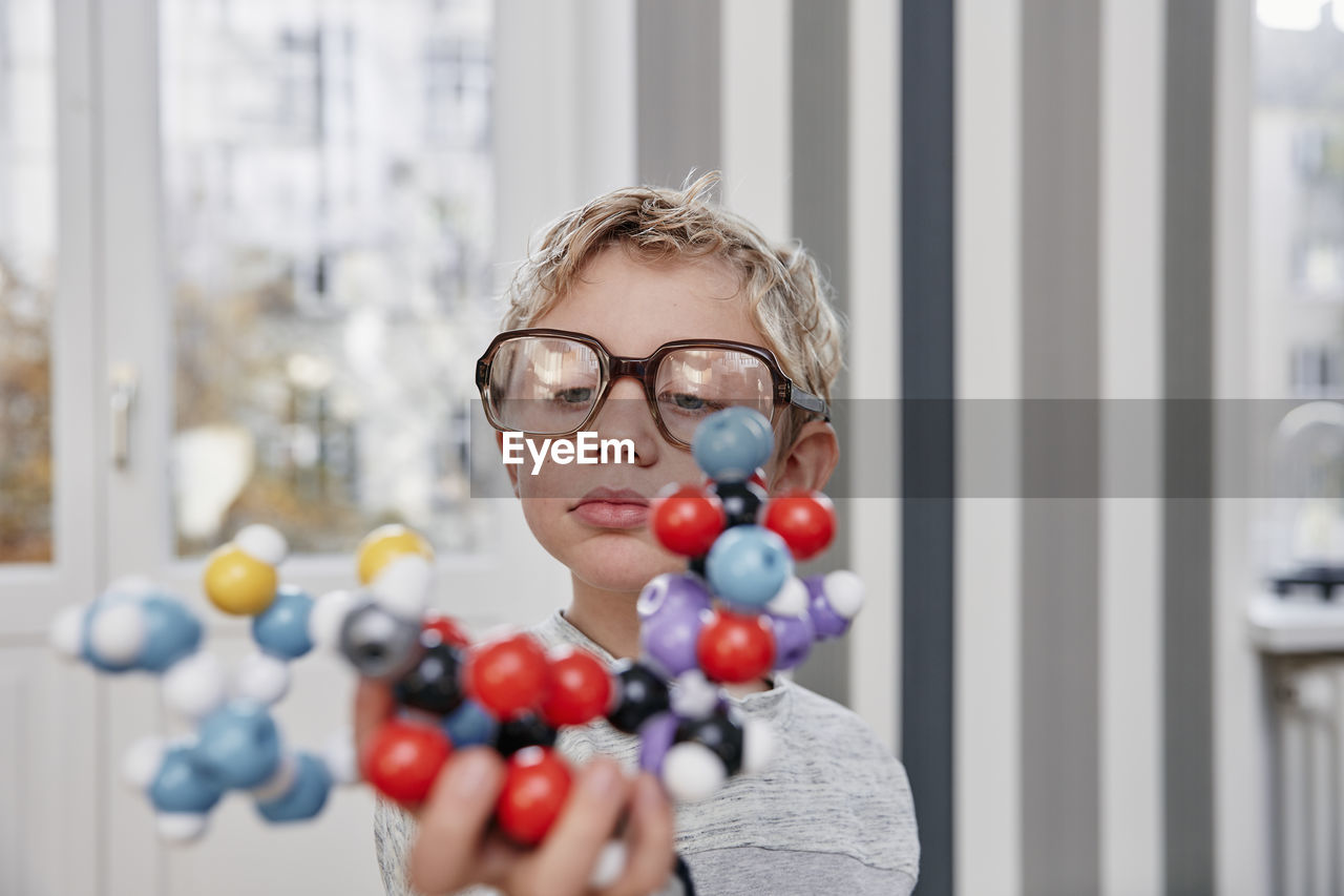 Boy wearing oversized glasses looking at molecular model