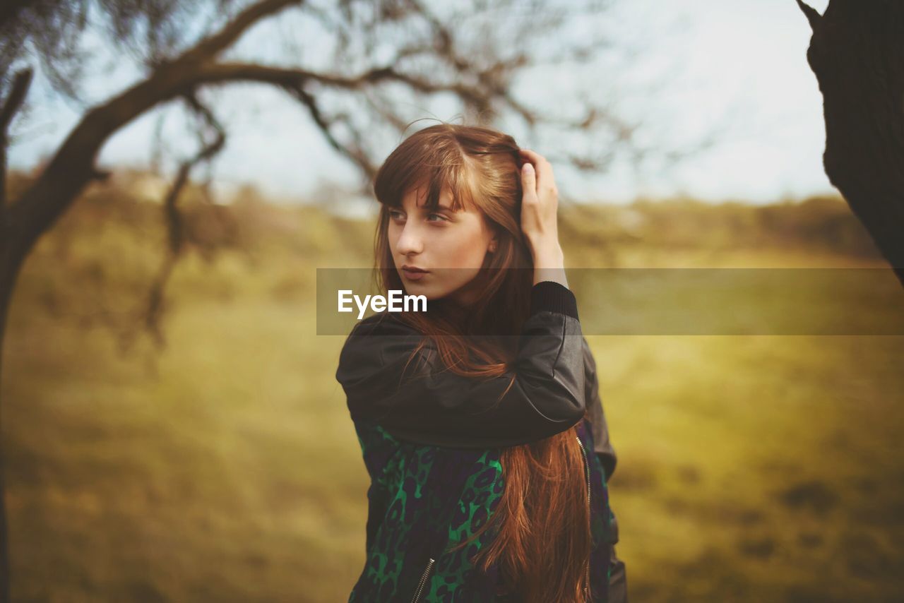 PORTRAIT OF YOUNG WOMAN STANDING ON TREE TRUNK