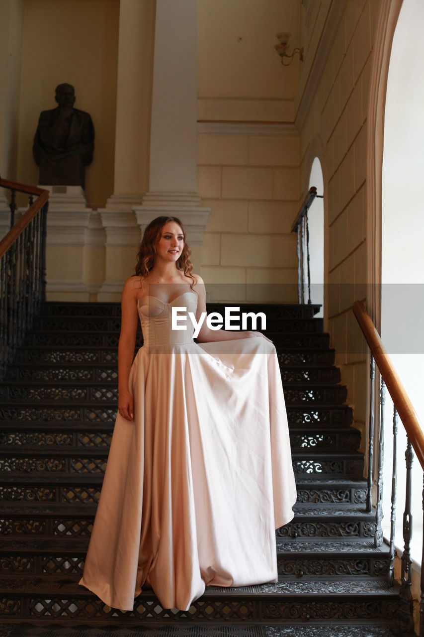 Smiling beautiful young woman wearing dress while standing on staircase