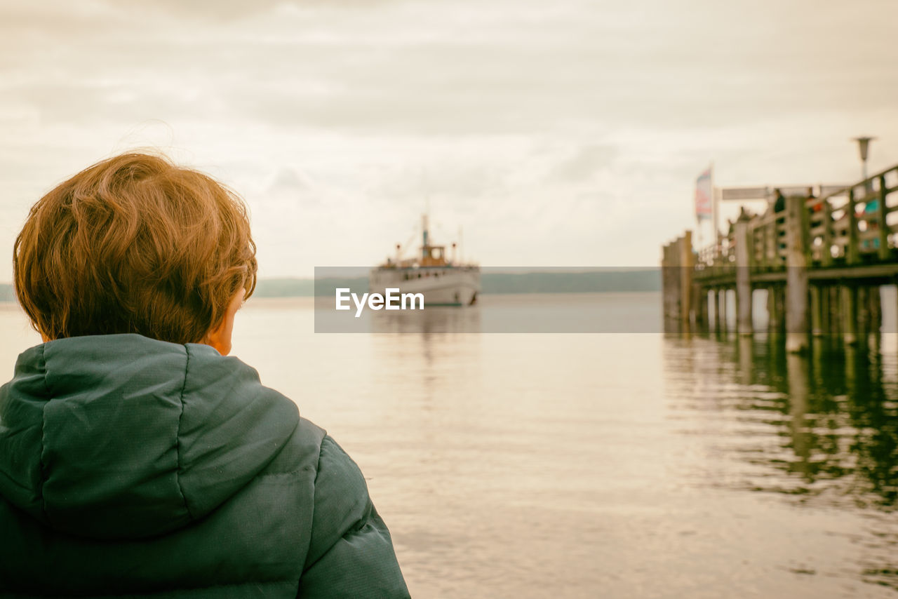 Rear view of boy looking at sea against sky during sunset