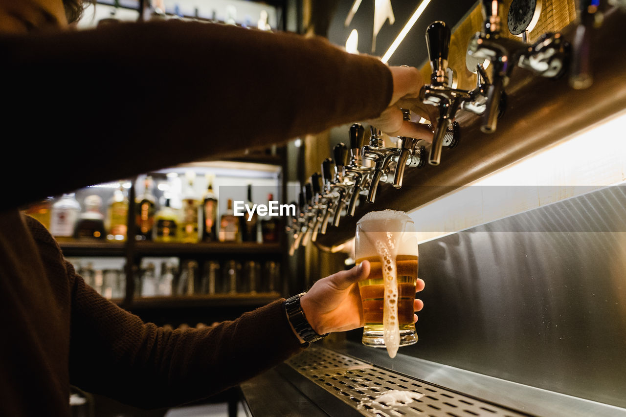 Cropped hands of bartender filling beer glass at bar