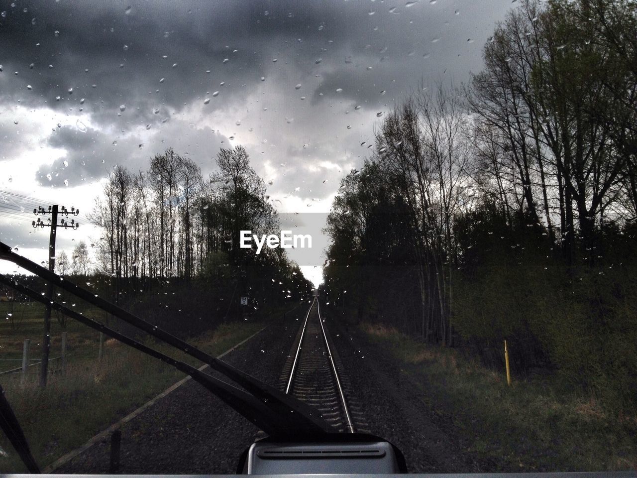 Railroad track amidst forest against cloudy sky in monsoon seen through train windshield